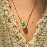 A necklace of a Pear-cut lagoon tourmaline with natural diamond and hand-carved 14K yellow gold Art Deco Style on neck