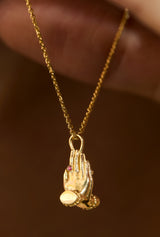 Sculpted praying hands charm in 14K gold on a fine chain, layered close-up