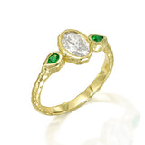 Organic 14K gold engagement ring featuring an oval diamond and two vivid green pear emeralds