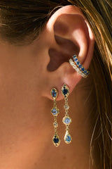 "Close-up of 14k gold hanging earrings with blue sapphires and diamonds worn in lobe, sapphire ear cuffs above"